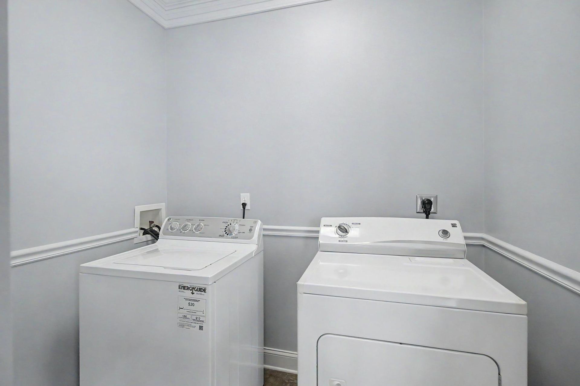 Pristine laundry room with side-by-side washer and dryer, soft gray walls, and crown molding