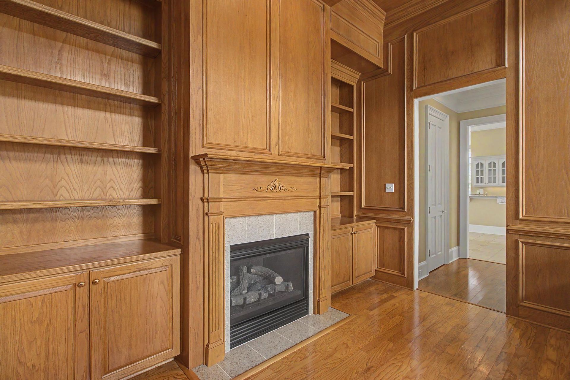 Detail of the paneled study showing a gas fireplace with white marble surround set into a wall of oak built-in bookshelves