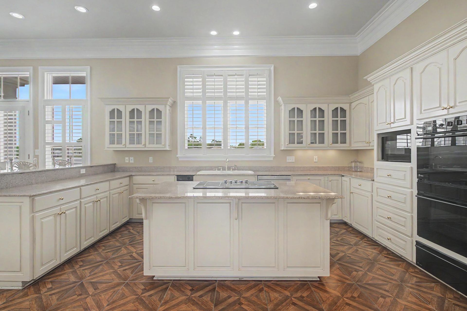 Chef's kitchen with a center island, painted cabinetry, parquet wood floors, and a wall of plantation-shuttered windows looking out toward the water