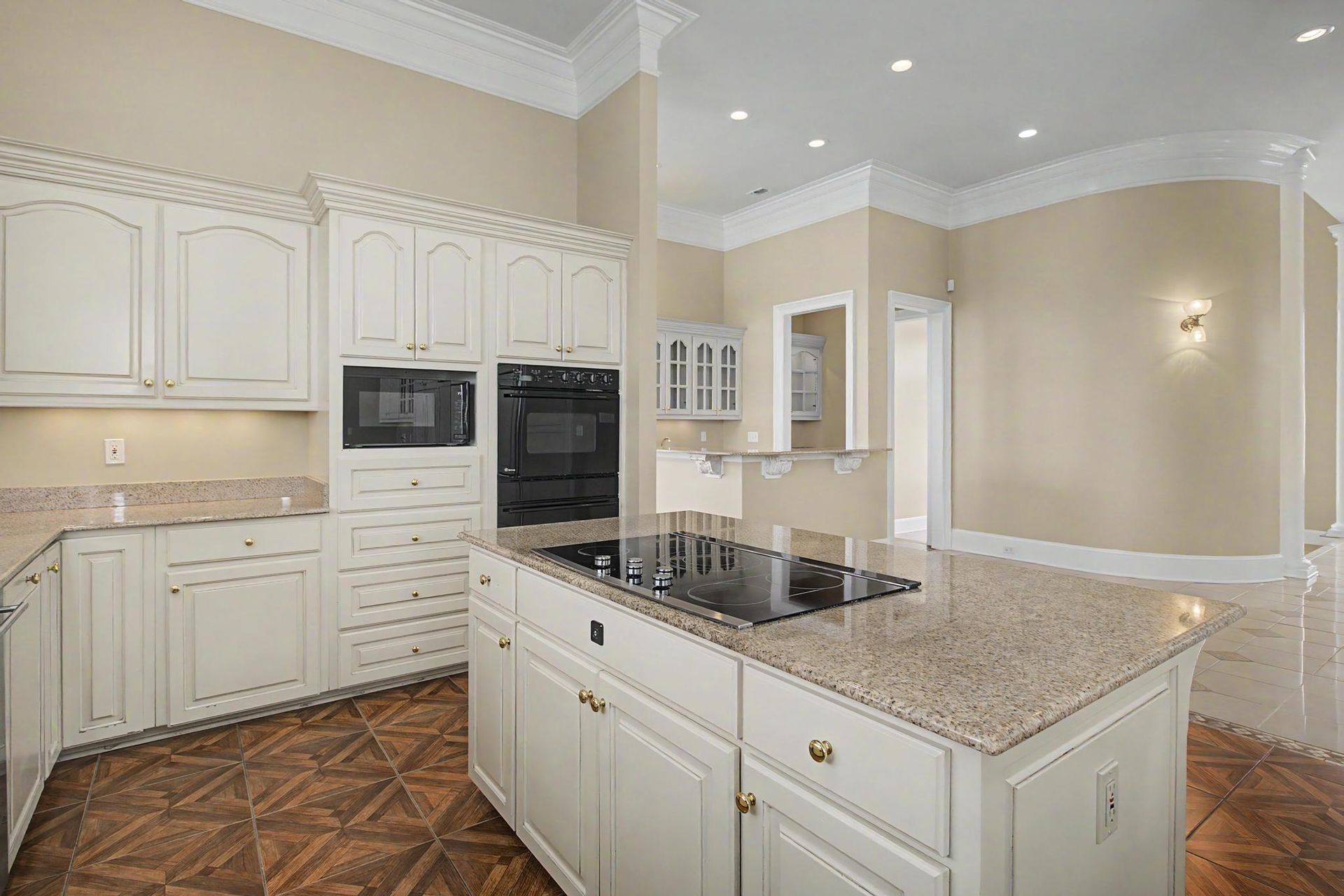 Wide angle of the chef's kitchen with double black ovens, a large island, granite countertops, and a curved hallway leading toward the entry