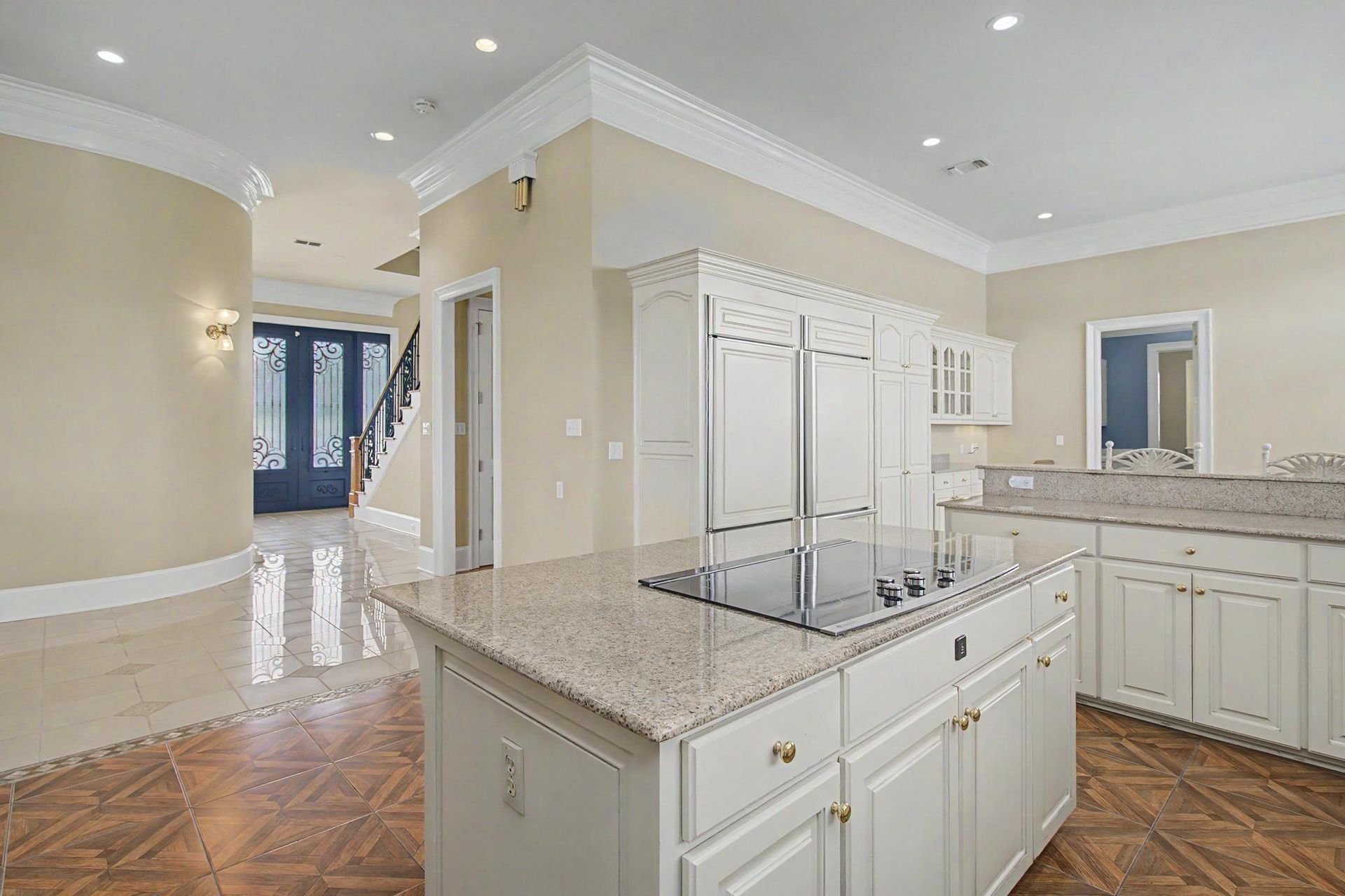 The kitchen opening into the foyer, with hardwood floors flowing into polished tile and the custom iron front doors visible in the distance