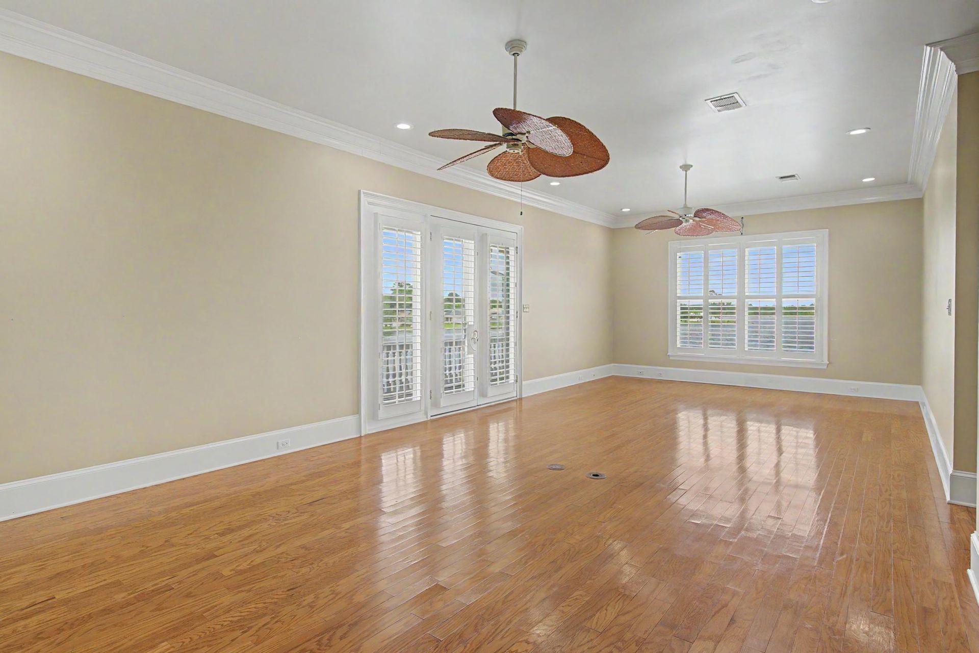A spacious bonus room with French doors opening to a balcony, hardwood floors, tropical-blade ceiling fans, and views of the bulkhead beyond